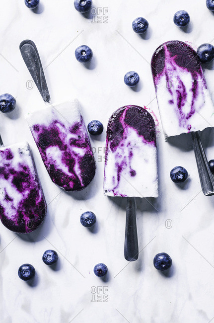 Blueberry coconut milk swirl popsicles with lime on marble background.