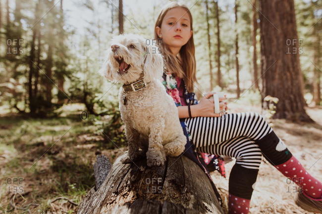 Girl sitting on log with white furry dog