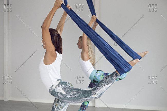Two women practicing aerial yoga in sunlit studio