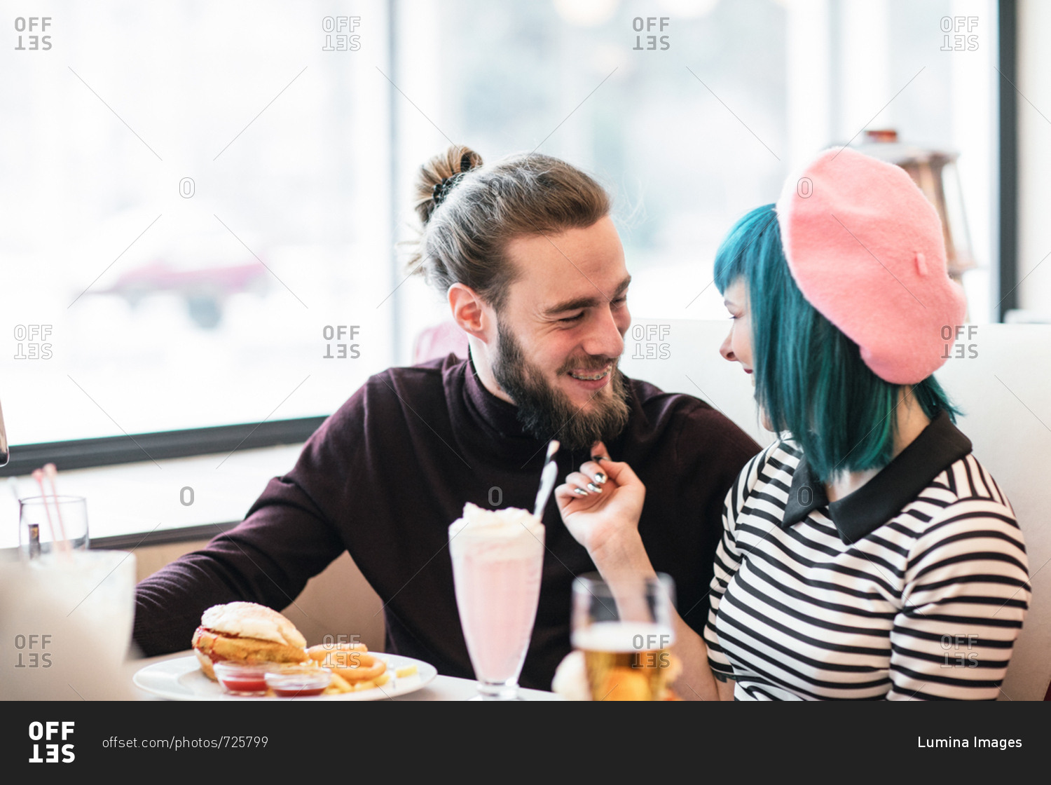 Young stylish man and woman in love eating vegetarian burgers an milkshake at vintage diner restaurant