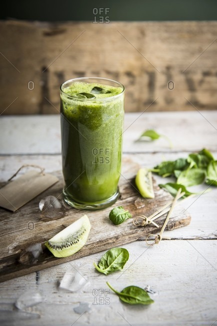 A glass of kiwi and spinach smoothie with fresh spinach leaves and slices of kiwi