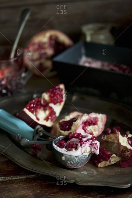 Fresh pomegranates and an ice cream scoop with pomegranate ice cream on a silver tray