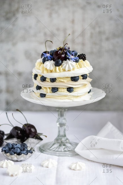 A meringue layer cake with whipped cream, lemon curd and berries on a cake stand