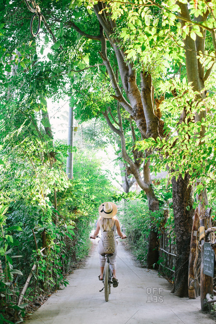 A blonde woman rides a beach bicycle down a village road
