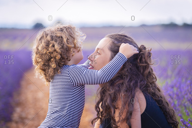 Side view of adult woman and little curly daughter together in blooming violet lavender field