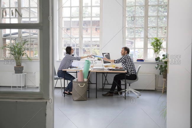 Man handing over folder to colleague at desk in a loft office