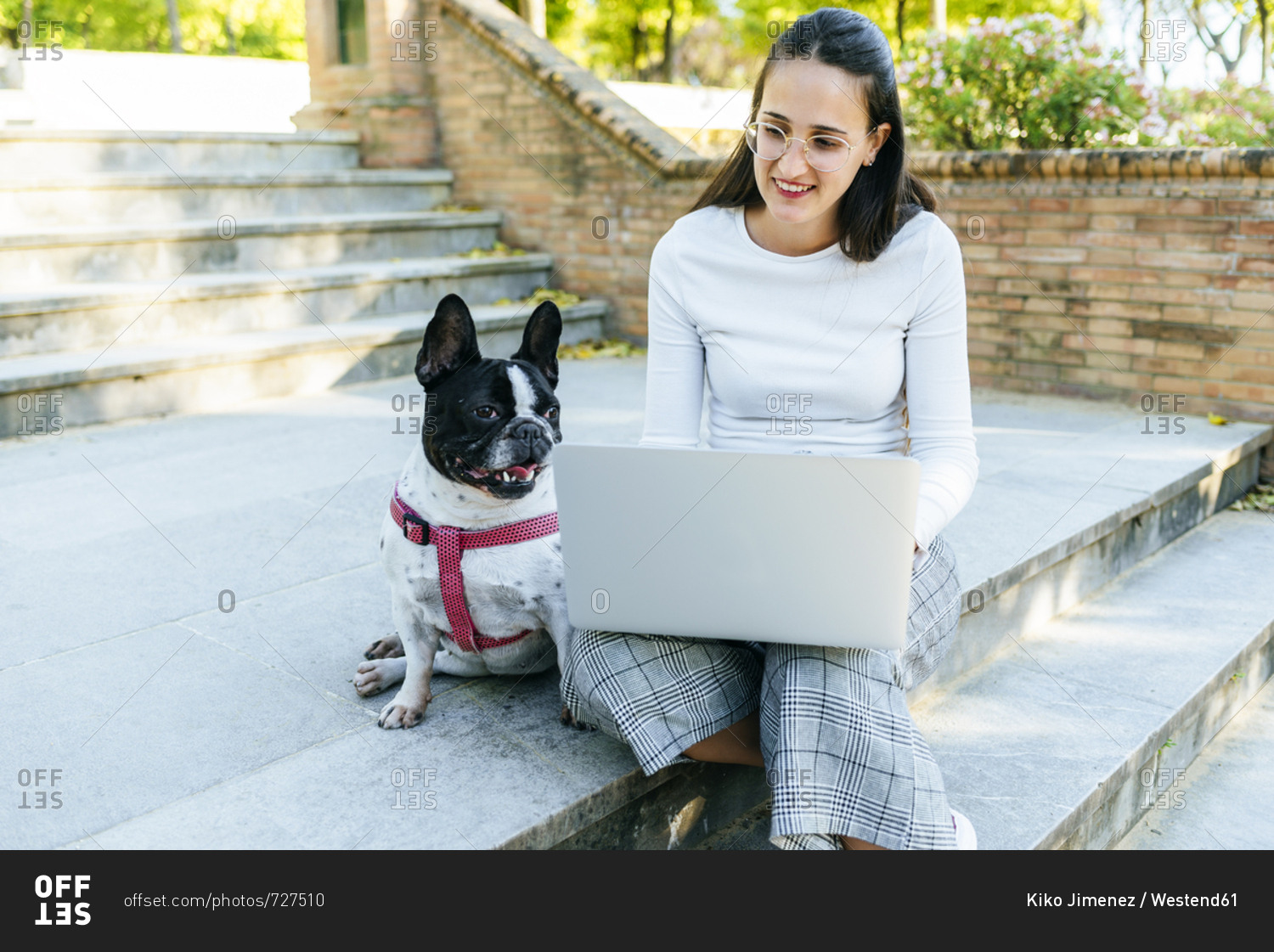 Woman using laptop next to her dog- sitting on stairs