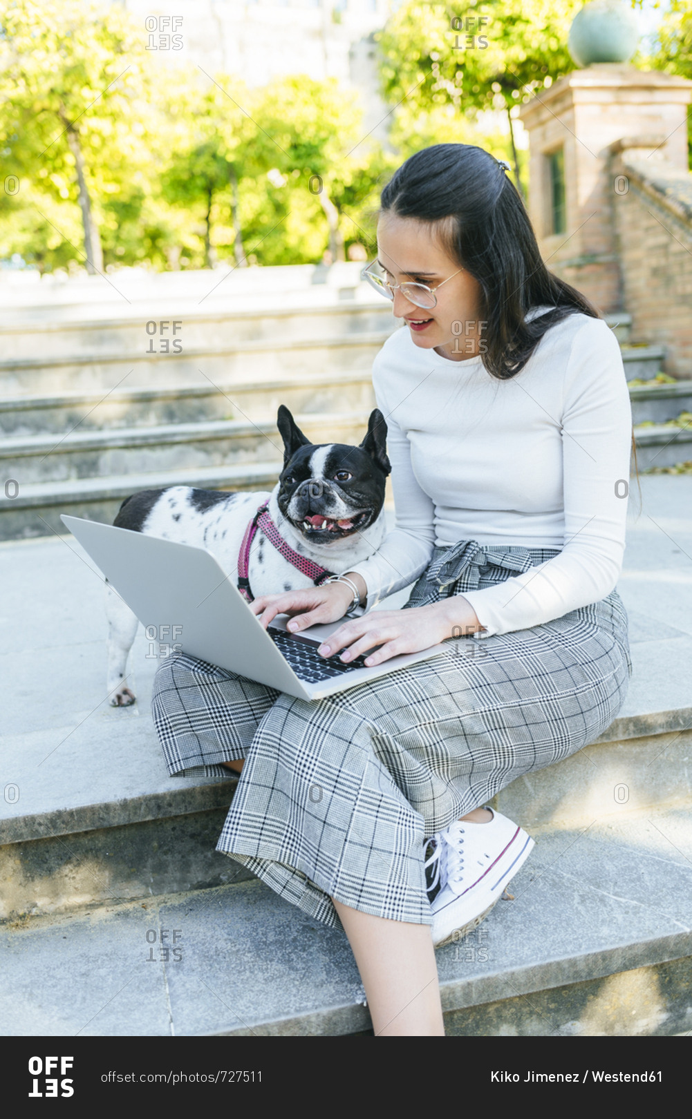 Woman using laptop next to her dog- sitting on stairs