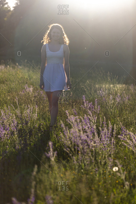 Young woman walking on flower meadow in the evening light