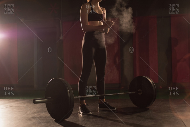 Woman rubbing powder on hand before barbell workout in gym