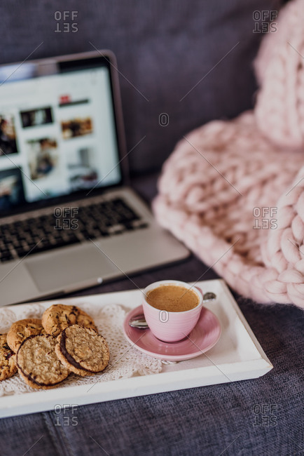 Tray with coffee and cookies in front of laptop on couch