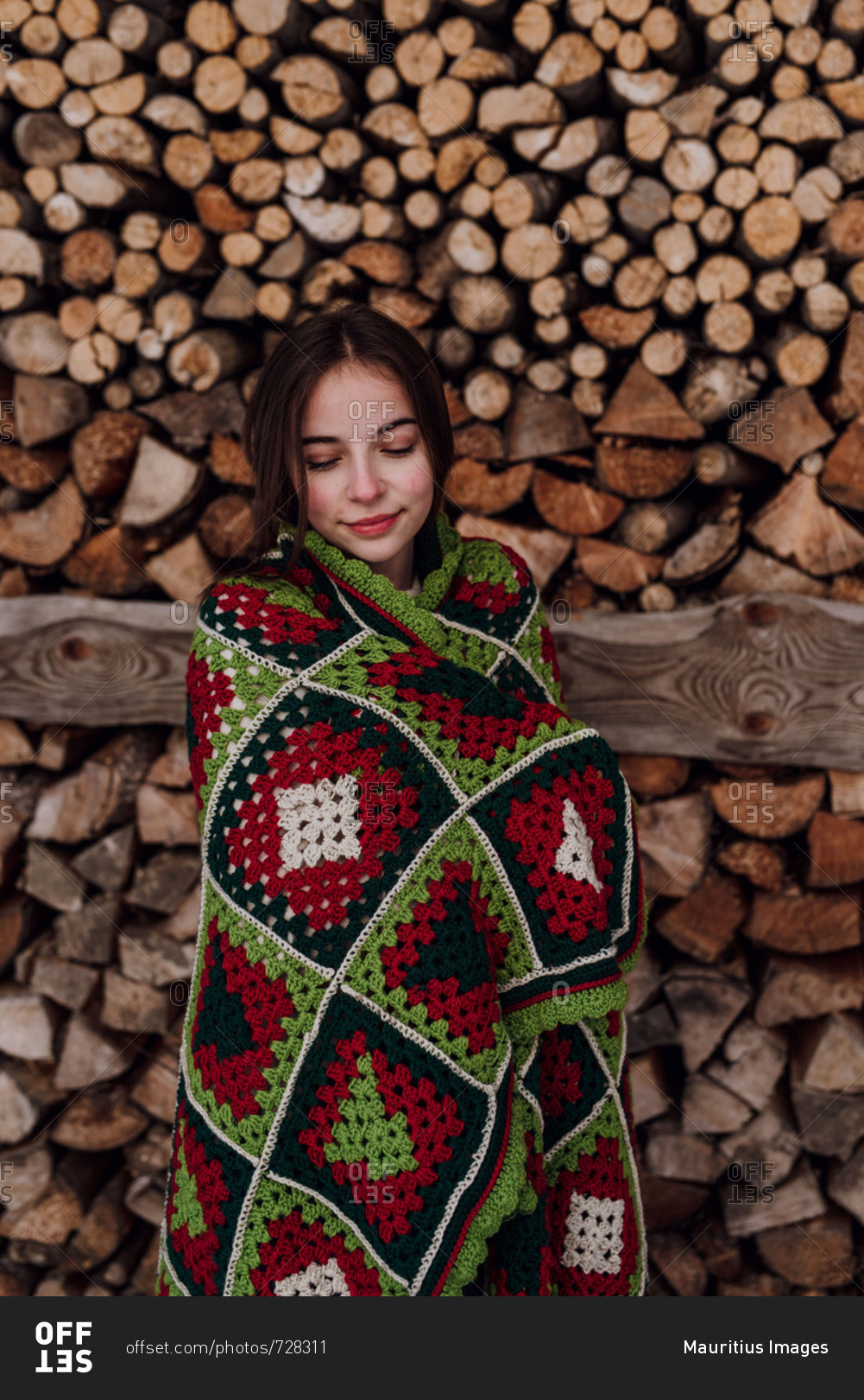 Young woman wrapped in a blanket in front of a woodpile stock photo