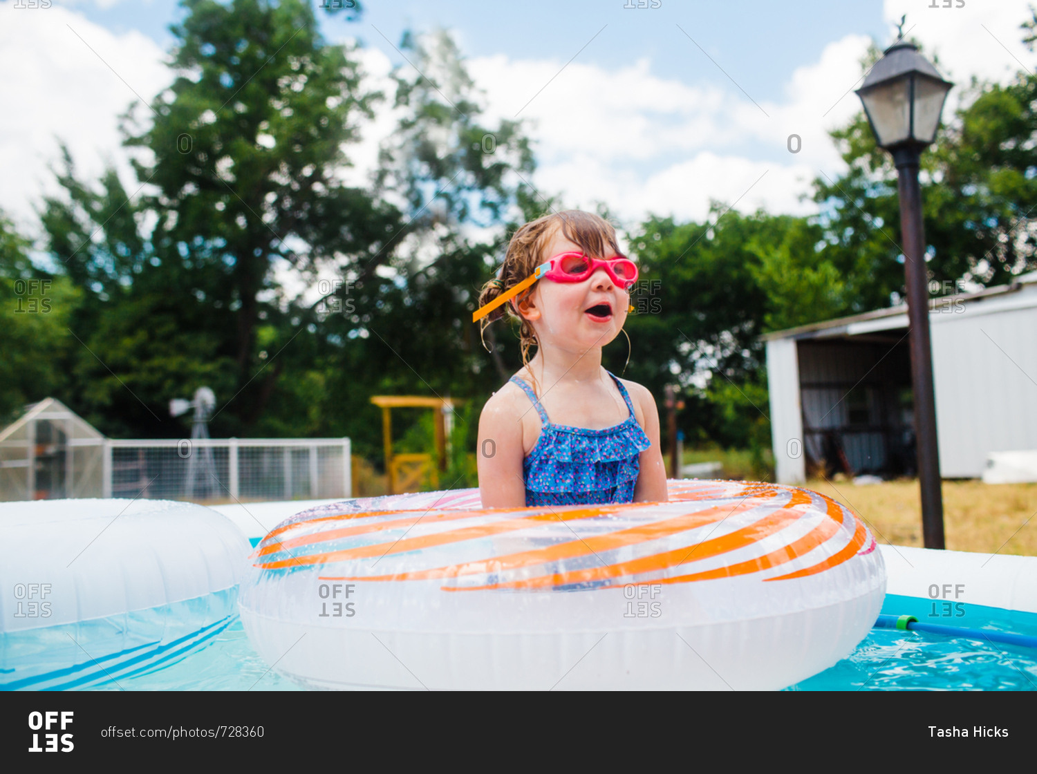 Young girl in backyard pool with inflatable rings stock photo - OFFSET