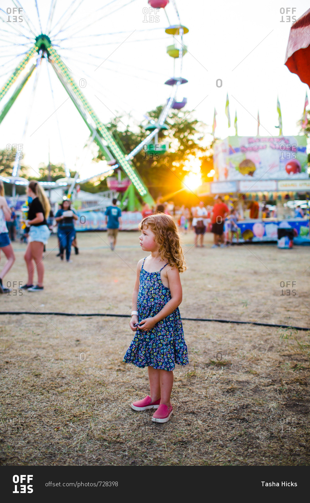 Young girl standing by big wheel at a fair at sunset
