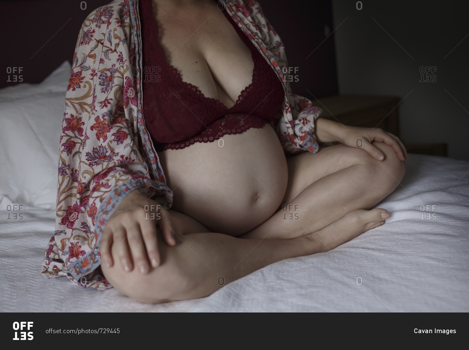 Low section of pregnant woman in lingerie sitting on bed in darkroom at home
