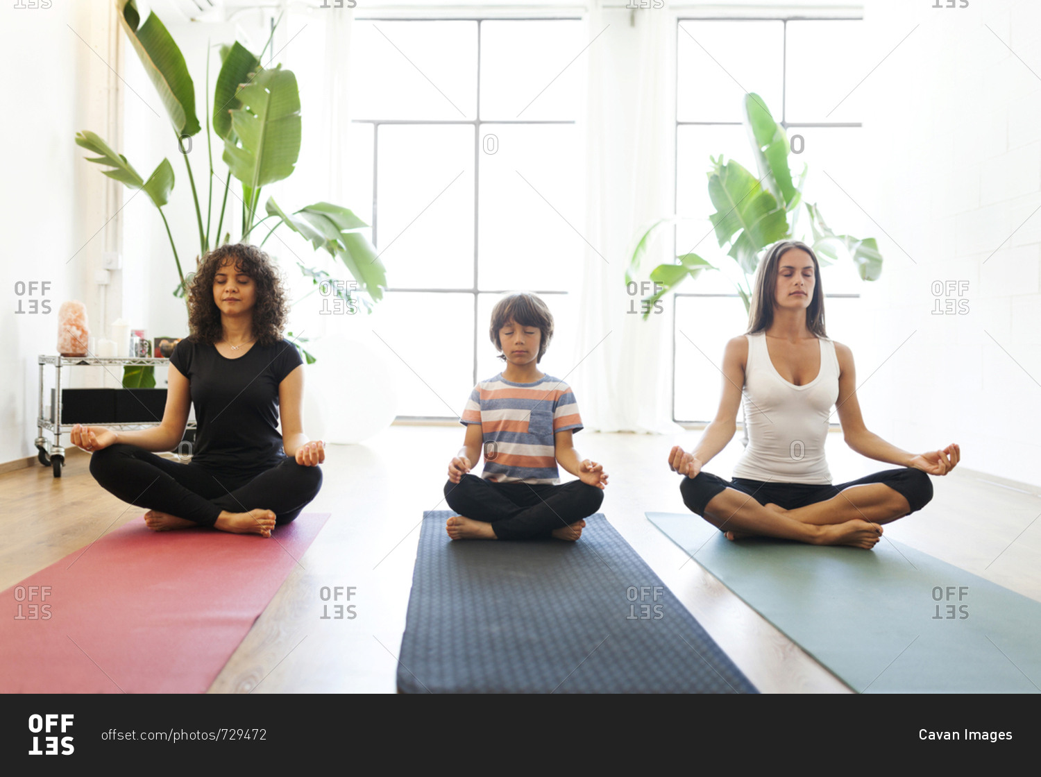 Female instructor with mother and son meditating against window in yoga studio