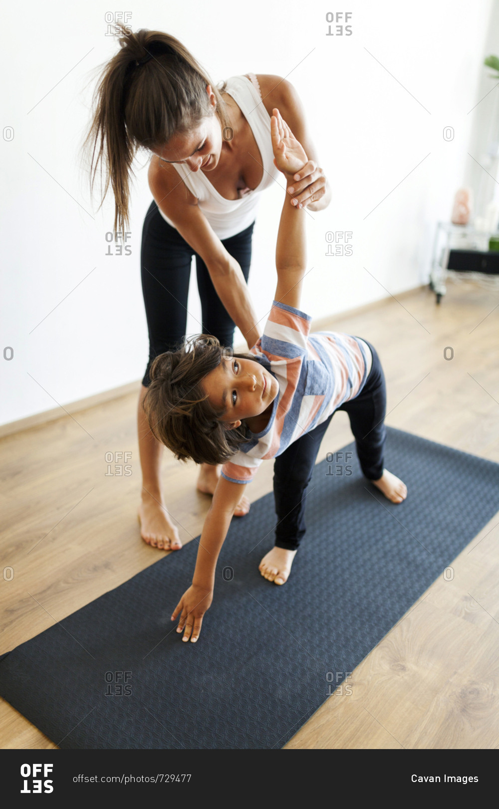 Yoga instructor assisting boy in exercising at yoga studio