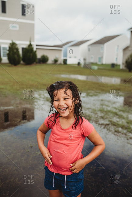 Laughing girl with wet messy hair playing in mud puddle