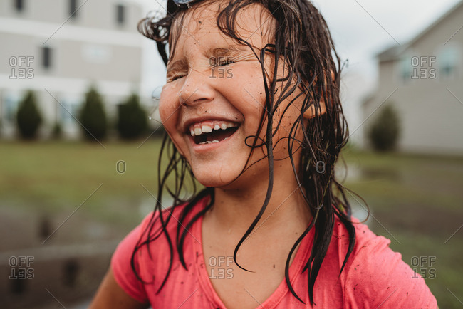 Portrait of a laughing girl with wet messy hair and dirty face playing in mud puddle