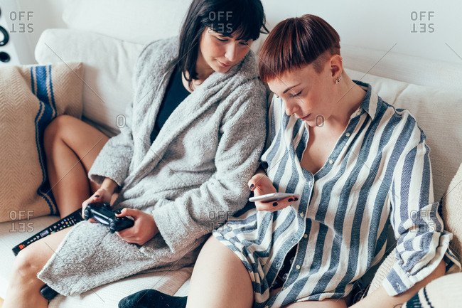 Women in nightwear relaxing on sofa looking at mobile phone