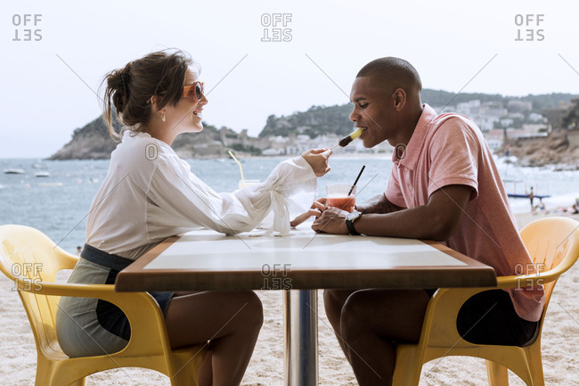 An interracial couple sharing a popsicle at a beach restaurant