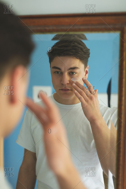 Man applying cream on face front of mirror at home