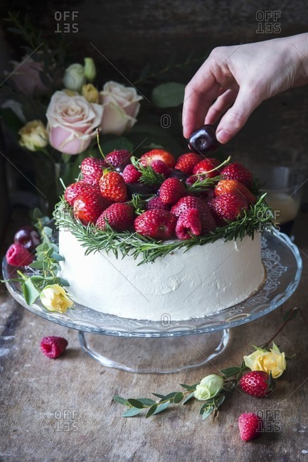 A vanilla buttercream cake garnished with red fruits and rosemary