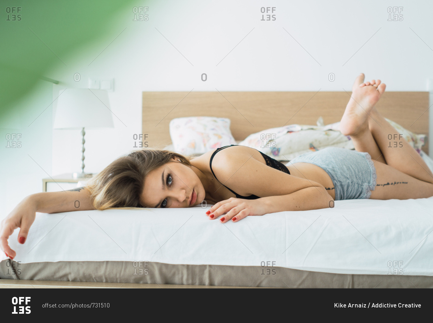 Blond woman in shorts and bra lying alone on bed looking sensually at  camera at home. stock photo - OFFSET