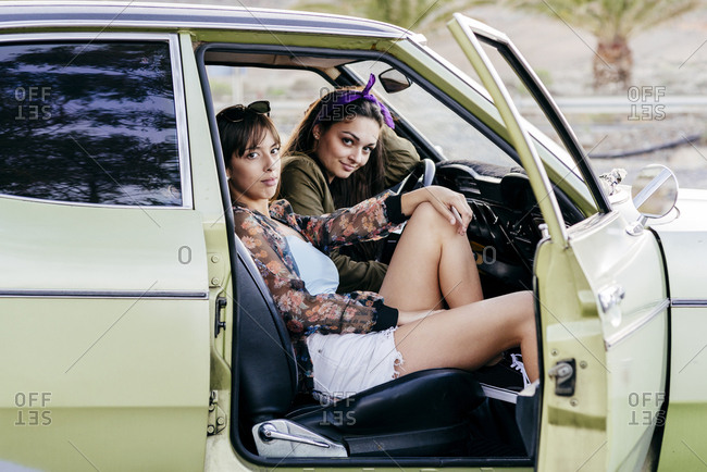 Side view of cool young glamour women sitting in green vintage muscle car and looking at camera.