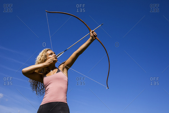 Archeress aiming with bow against blue sky