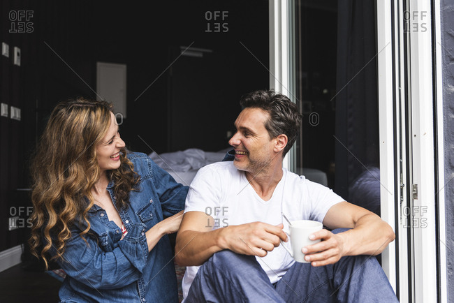 Happy couple in nightwear at home sitting at French window