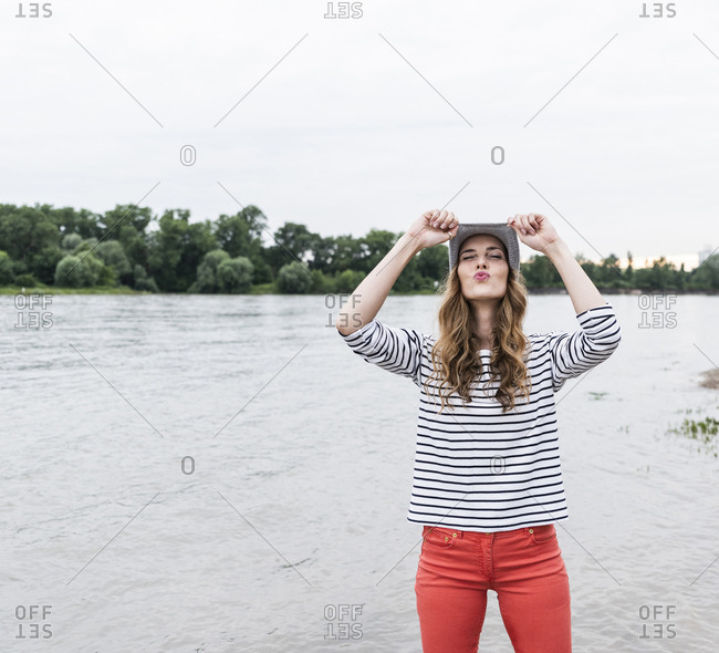 Playful woman wearing wooly hat at a river pouting