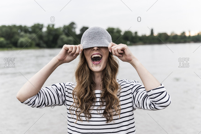 Laughing woman playing with wooly hat at a river