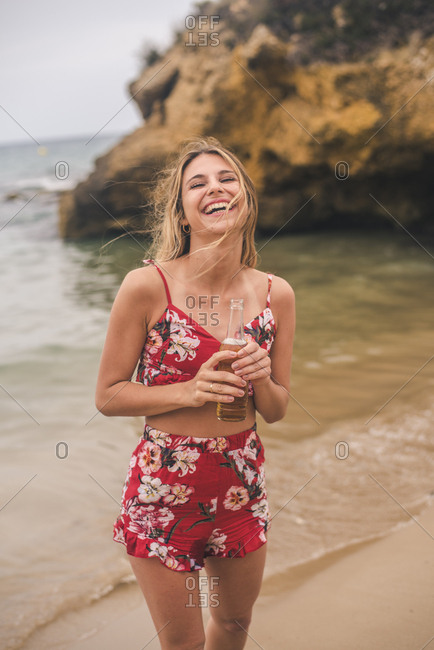 Portrait of happy young woman standing with a beer on the beach