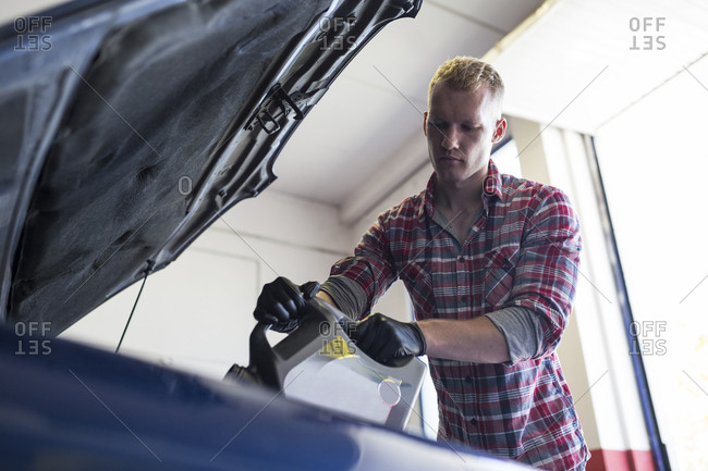 Man in gloves holding can of engine oil and pouring it through funnel into car
