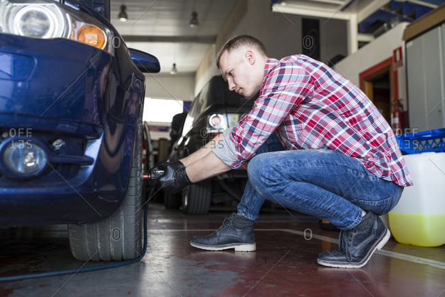 Side view of man tightening lug nuts on car wheel with electric screwdriver