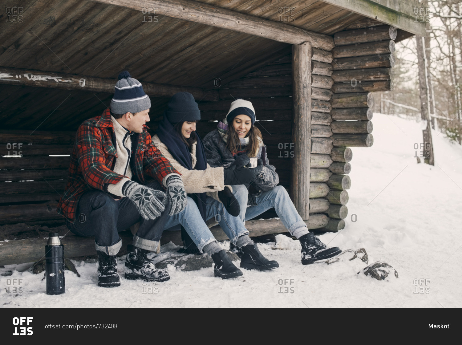 Friends sharing drink while sitting at log cabin during winter