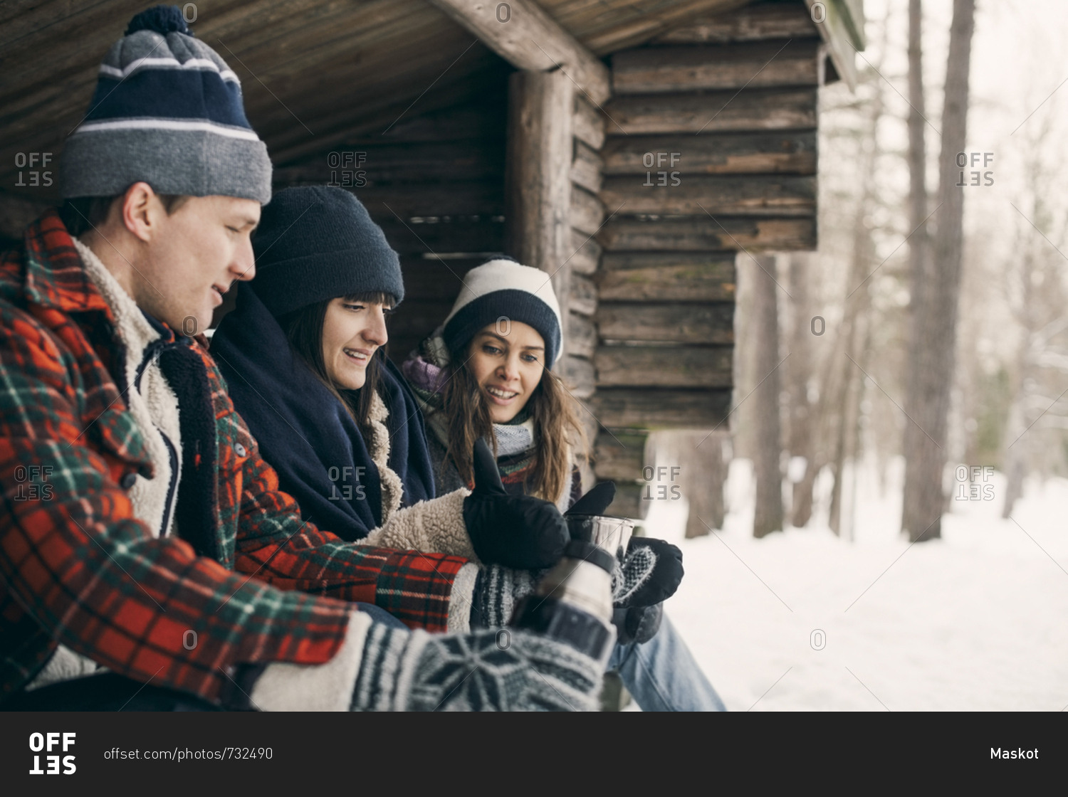 Man giving drink to female friends while sitting at log cabin during winter