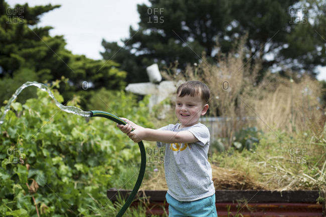 Boy plays with garden hose in the summer heat