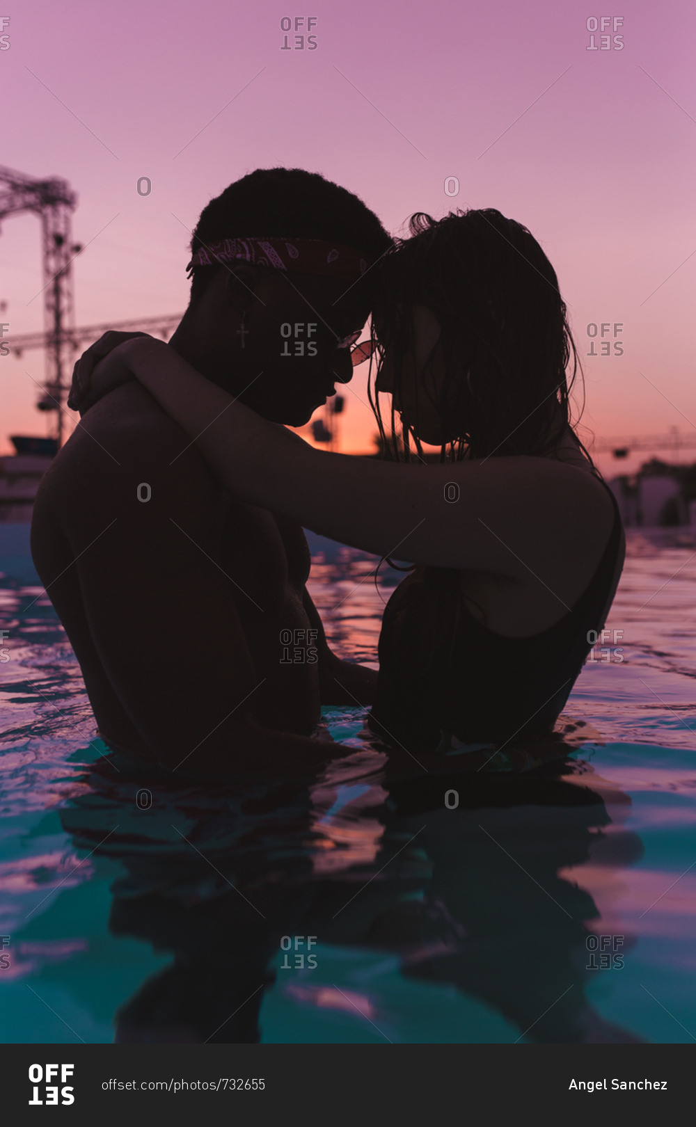 Side view of silhouette of mixed race couple embraced on the swimming pool in a purple sunset of summer