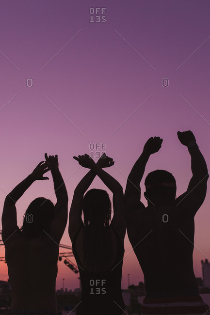 Three friends putting up their hands in a purple sunset of summer