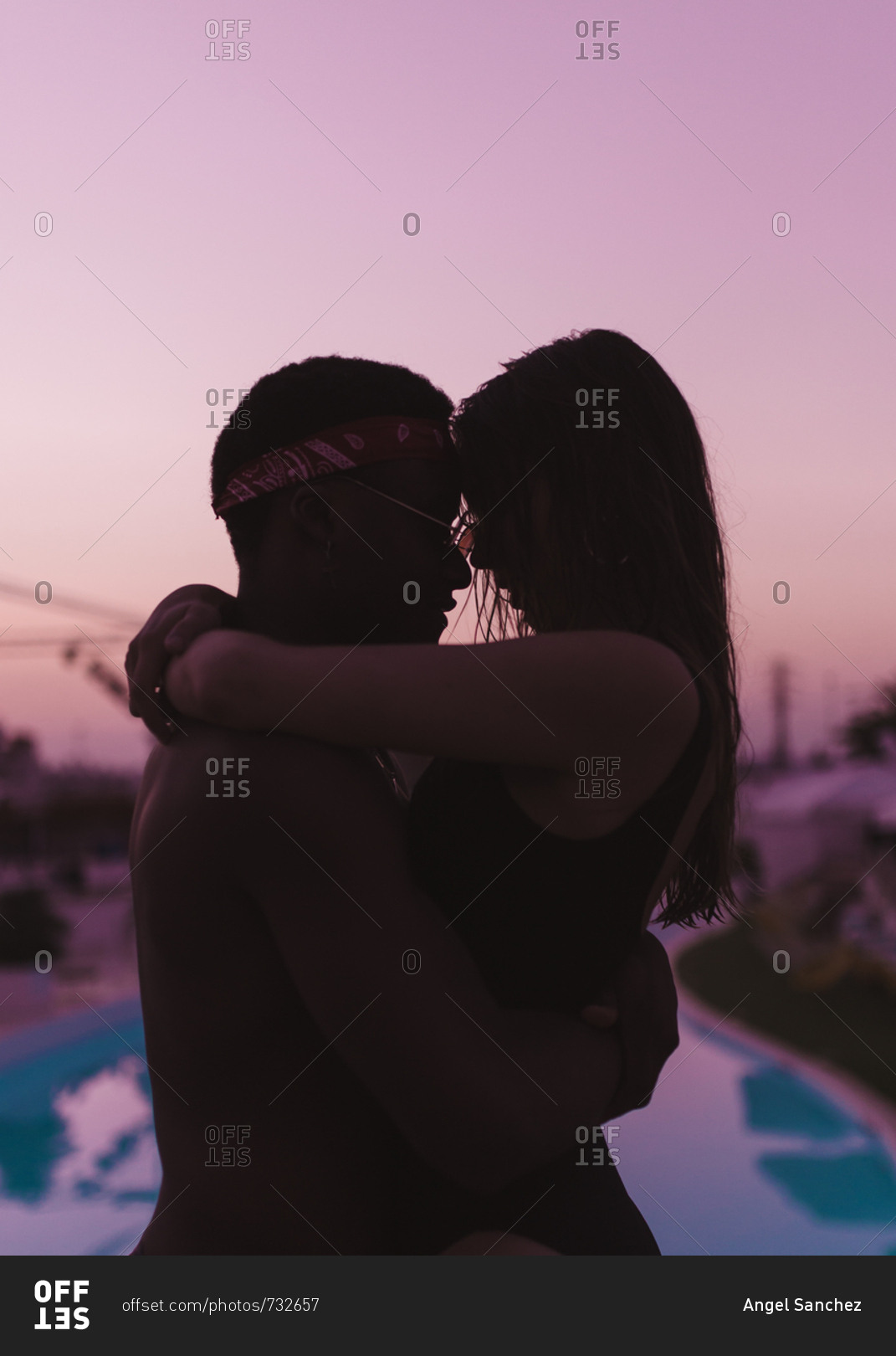 Side view of silhouette of mixed race couple embraced on the swimming pool in a purple sunset of summer