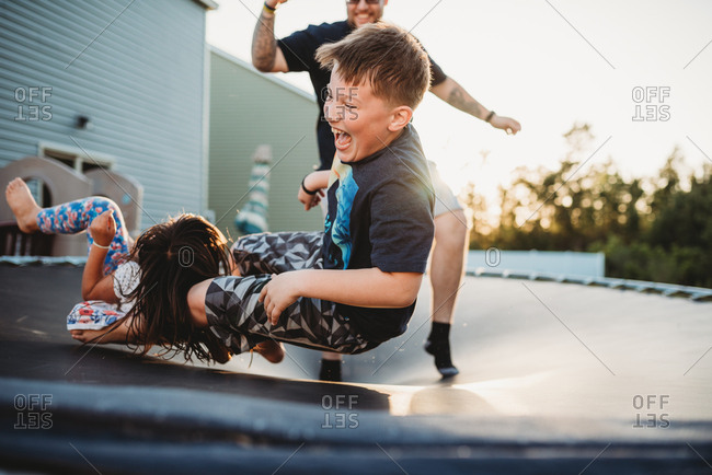 Laughing boy bouncing on trampoline with his father and sister
