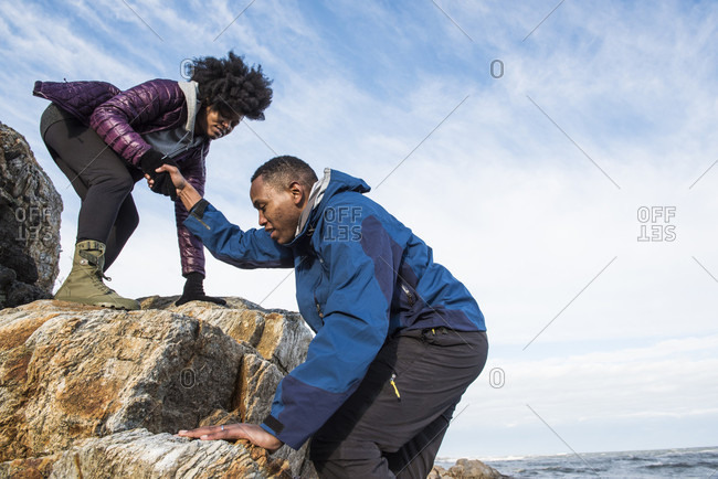 Woman helping man up rock outcrop, Kittery, Maine, USA