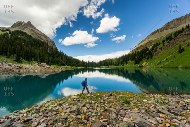 Man hikes along the shore of blue lake with reflection in the San Juan Mountains of Colorado