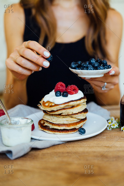 Woman adding blueberries to stack of pancakes