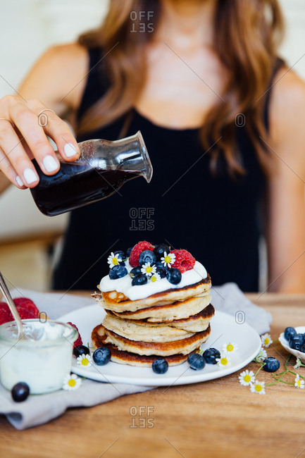 Woman pouring syrup on stack of pancakes