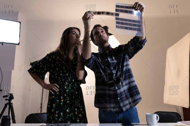 Male photographer and female model looking at negative filmstrip in photo studio