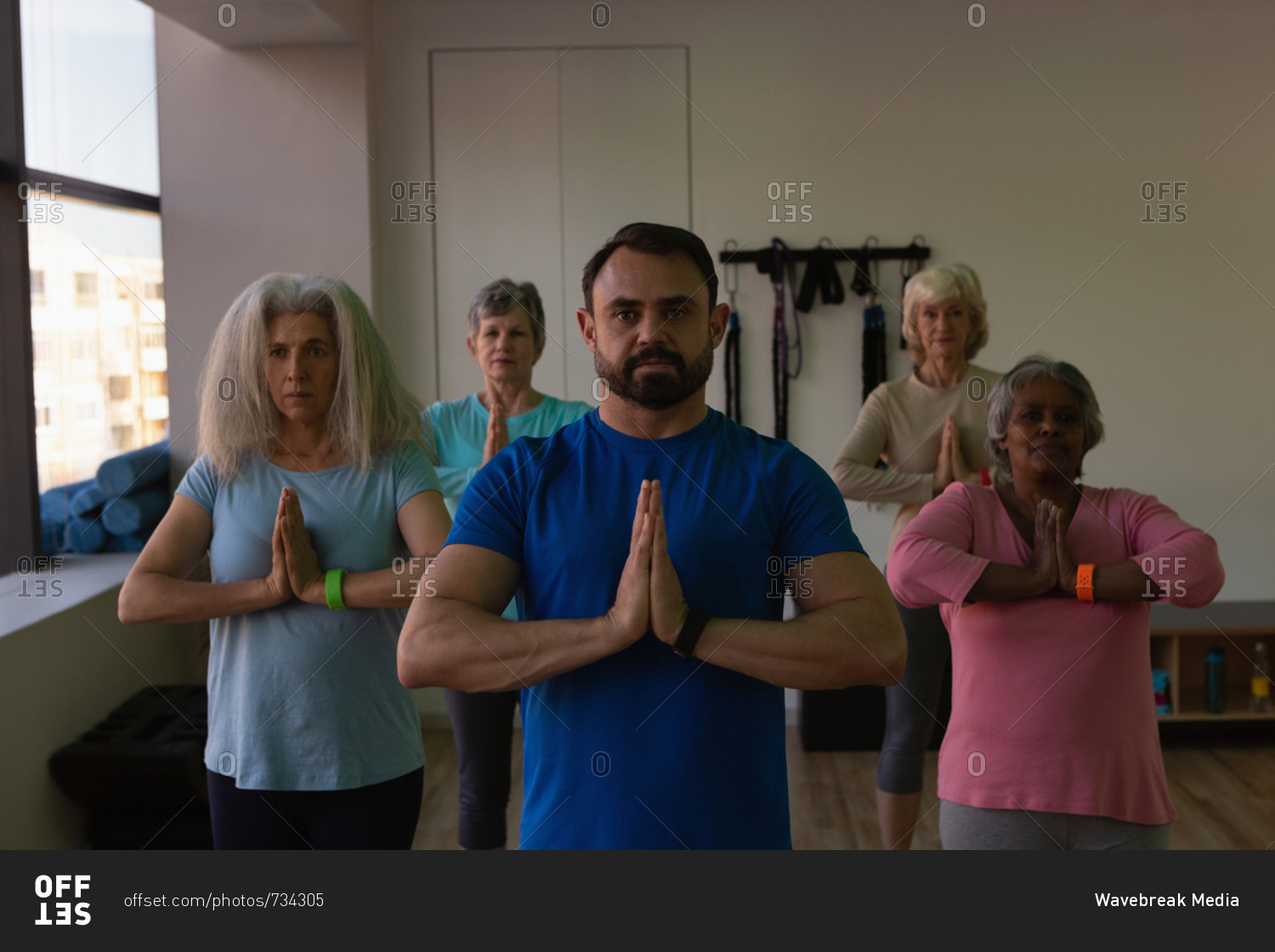 Trainer and group of senior women performing yoga in yoga center