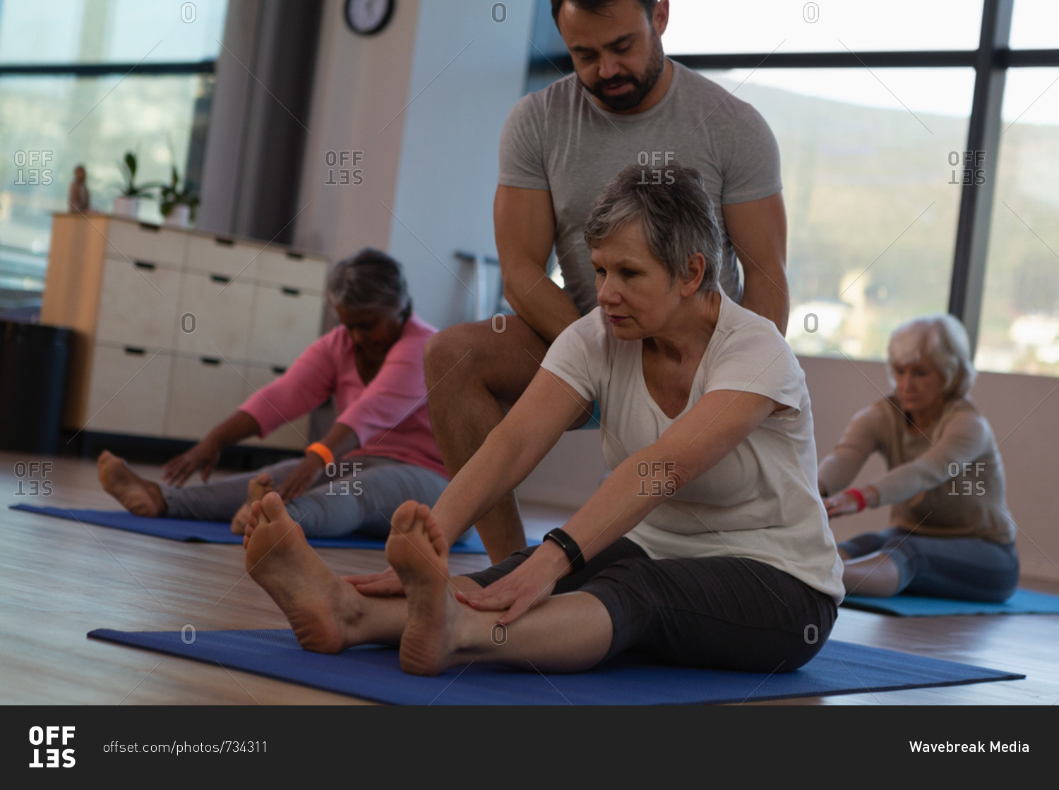 Trainer assisting senior women in performing yoga at yoga center